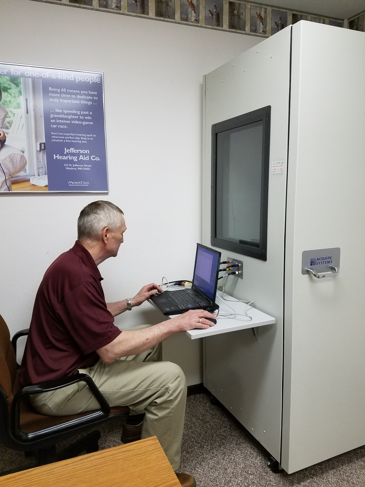 hearing specialist working at laptop in front of hearing test booth window